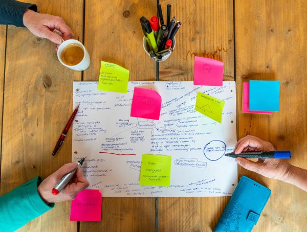 foto van de handen van twee mensen die schrijven en post-its plakken in een creatief proces. Nanda Niemeijer aan het werk met een klant om goed onderwijs te ontwerpen.